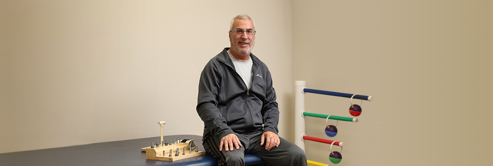 A man wearing a tracksuit sitting on a padded table in a physical therapy room
